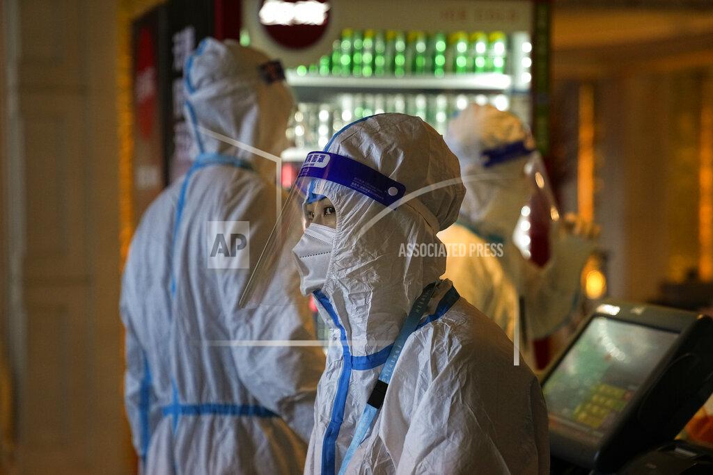 Three hotel workers in protective gear stand next to a checkout stand at the Shangri-La Hotel at the 2022 Winter Olympics, Wednesday, Feb. 16, 2022, in Beijing. (AP Photo/Jae C. Hong)