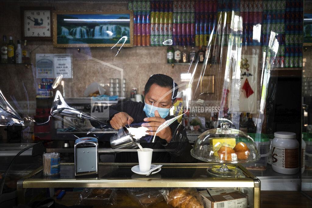 Bernat Armangue A waiter wearing a face mask and behind a plastic curtain to prevent the spread of coronavirus serves a coffee at a bar in the southern neighbourhood of Vallecas in Madrid, Spain, Tuesday, Sept. 22, 2020. Madrid is poised to extend its restrictions on movement to more neighborhoods, due to a surge in new cases in other districts and despite an outcry from residents over discrimination. Police on Monday deployed to 37 working-class neighborhoods that have seen 14-day transmission rates above 1,000 per 100,000 inhabitants. (AP Photo/Bernat Armangue)