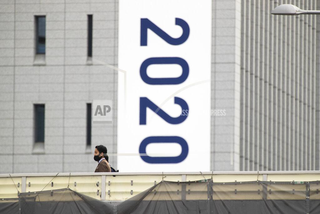 Hiro Komae People wearing face masks walk on a crossover bridge near a banner to promote the rescheduled Tokyo 2020 Olympic Games in Tokyo Friday, April 2, 2021. Many preparations are still up in the air as organizers try to figure out how to hold the postponed games in the middle of a pandemic. (AP Photo/Hiro Komae)