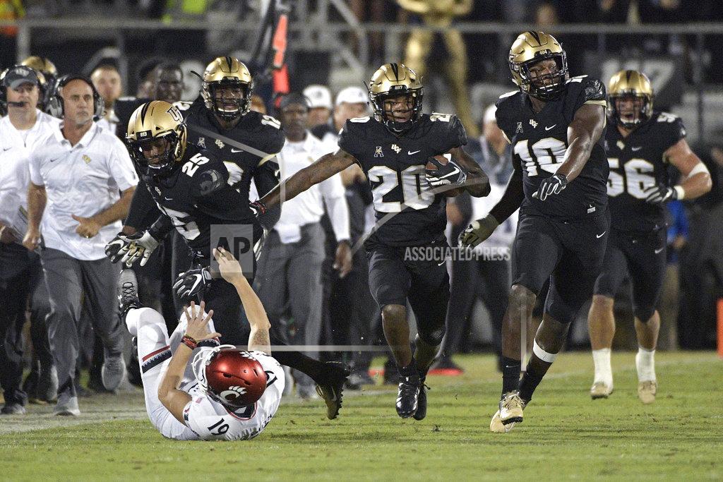 Phelan M. Ebenhack Central Florida defensive back Brandon Moore (20) returns a blocked punt 60-yards as defensive lineman Titus Davis (10) helps and defensive back Kyle Gibson (25) blocks Cincinnati place kicker Cole Smith (19) during the first half of an NCAA college football game Saturday, Nov. 17, 2018, in Orlando, Fla. (AP Photo/Phelan M. Ebenhack)