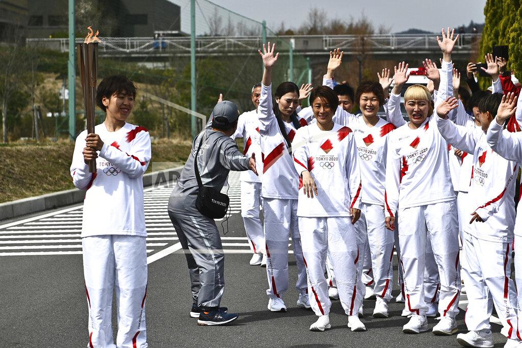Japanese torchbearer Azusa Iwashimizu, left, a member of Japan women's national football team, smiles after passing the flame to the next torchbearer during the torch relay grand start outside J-Village National Training Center in Naraha, Fukushima prefecture, northeastern Japan, Thursday, March 25, 2021. The torch relay for the postponed Tokyo Olympics began its 121-day journey across Japan on Thursday and is headed toward the opening ceremony in Tokyo on July 23. (Philip Fong/Pool Photo via AP)