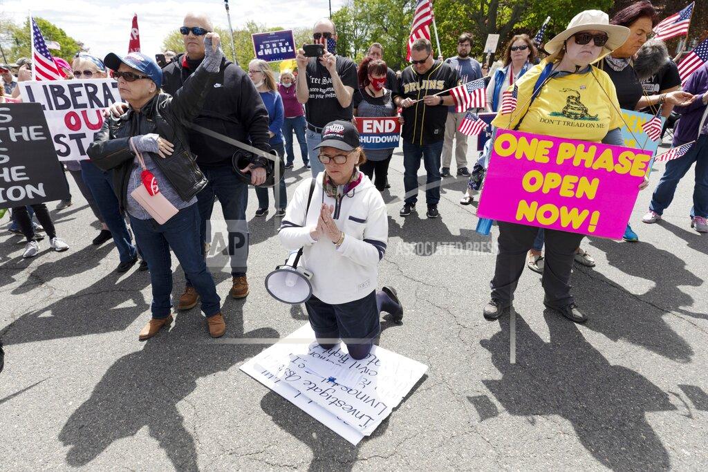 Michael Dwyer A woman kneels in prayer during a demonstration against state restrictions over concern about COVID-19 near the residence of Gov. Charlie Baker, Saturday, May 16, 2020, in Swampscott, Mass. (AP Photo/Michael Dwyer)