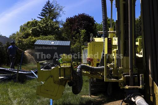 A Dandelion Energy employee sprays excess groundwater back on the lawn during installation of a geothermal heat pump system at a home in White Plains, N.Y., Monday, May 8, 2023. A water-filled loop is installed several hundred feet deep in the yard to either carry heat away from or into the house depending on season. Industry experts see the technology becoming increasingly popular in the coming years. (AP Photo/Julia Nikhinson)