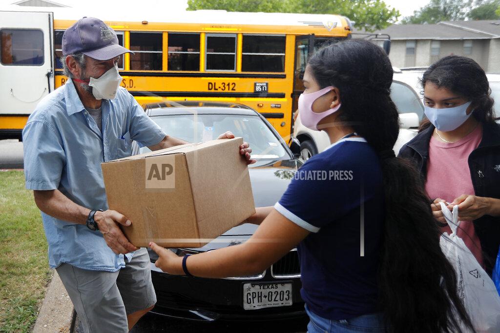 Berkner High School soccer coach, Denny Gunnerson, left, hands out a box of food at a food distribution site in an apartment complex in Dallas, Friday, May 15, 2020. Cafe Momentum has been delivering 1,550 meal kits a week to families in the area through various groups. Most of the kits, which include four meals for a family of four, are being distributed in the Richardson Independent School District. (AP Photo/Tony Gutierrez)