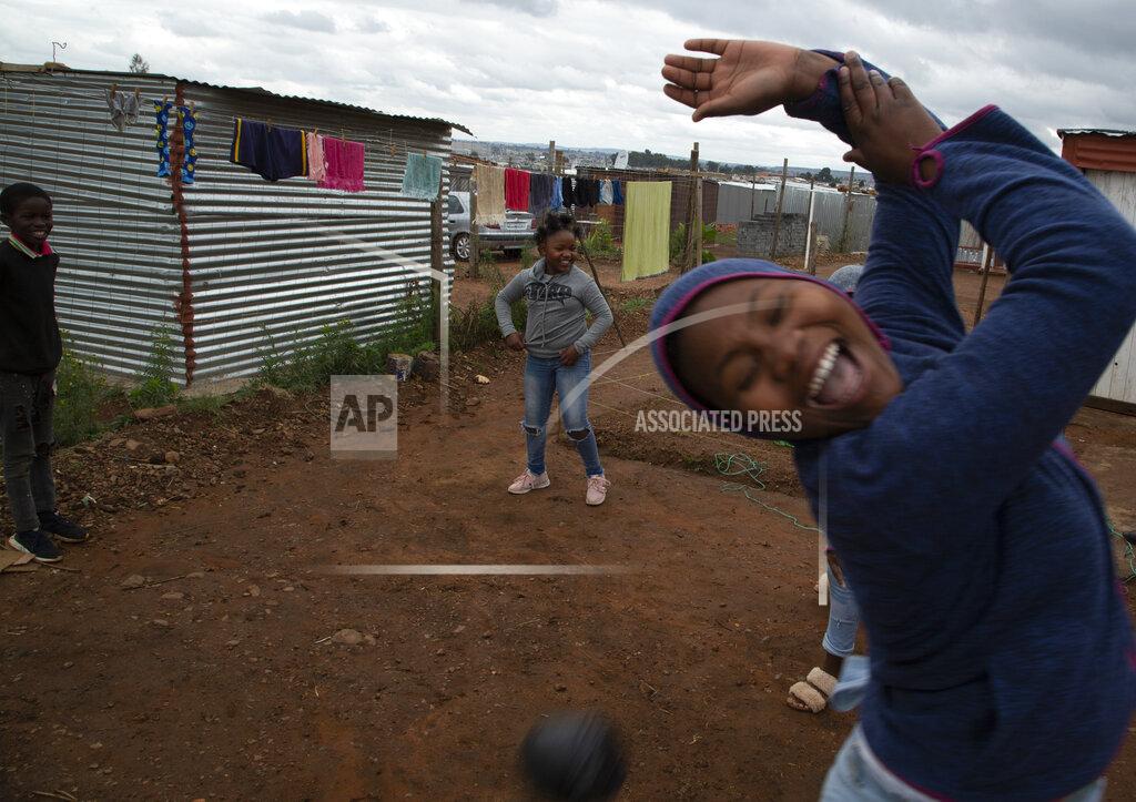 Lilitha Jiphethu, 11, background center, plays with her friends with a ball made from discarded plastic grocery bags, outside her home in Orange Farm, South Africa, on Tuesday, April 28, 2020. Like many children under lockdown, she misses her friends and her teachers, but understands why school is closed and why they are being kept at home. (AP Photo/Denis Farrell)