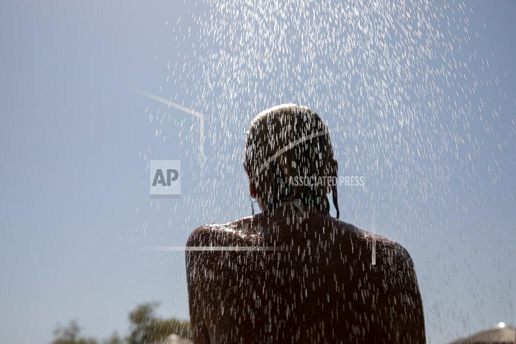 Yorgos Karahalis A woman takes a shower at a beach of Lagonissi village, a few miles southwest of Athens, on Thursday, July 29, 2021. One of the most severe heat waves recorded since 1980s scorched southeast Europe on Thursday, sending residents flocking to the coast, public fountains and air-conditioned locations to find some relief, with temperatures rose above 40 C (104 F) in parts of Greece and across much of the region. (AP Photo/Yorgos Karahalis)