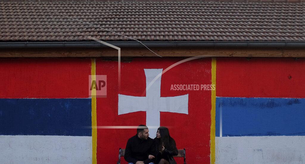 Darko Vojinovic In this photo taken Monday, Feb. 17, 2020, a couple waits at a bus station by graffiti that shows Serbian flag, left, Montenegrin war flag, center, and old Montenegro flag, right, in Belgrade, Serbia. Montenegro's President Milo Djukanovic says the upcoming parliamentary vote is crucial in the defense of the small Balkan country's independence in the face of renewed attempts from Serbia and Russia to install their nationalist and anti-Western allies to power. (AP Photo/Darko Vojinovic)