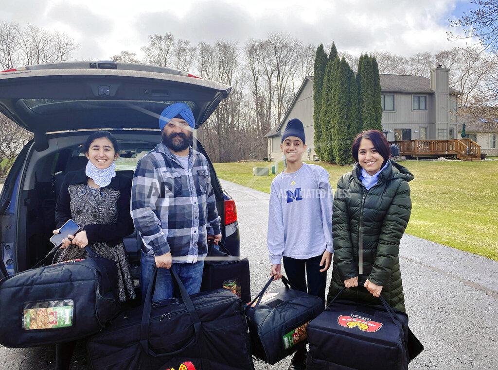 In this April 1, 2020 photo provided by Paramjyoti Kaur Singh, Singh family members Baani, Shalinder, Arjun and Jasveen Kaur pose for a photo before delivering pizzas to health care workers in Detroit. (Paramjyoti Kaur Singh via AP)