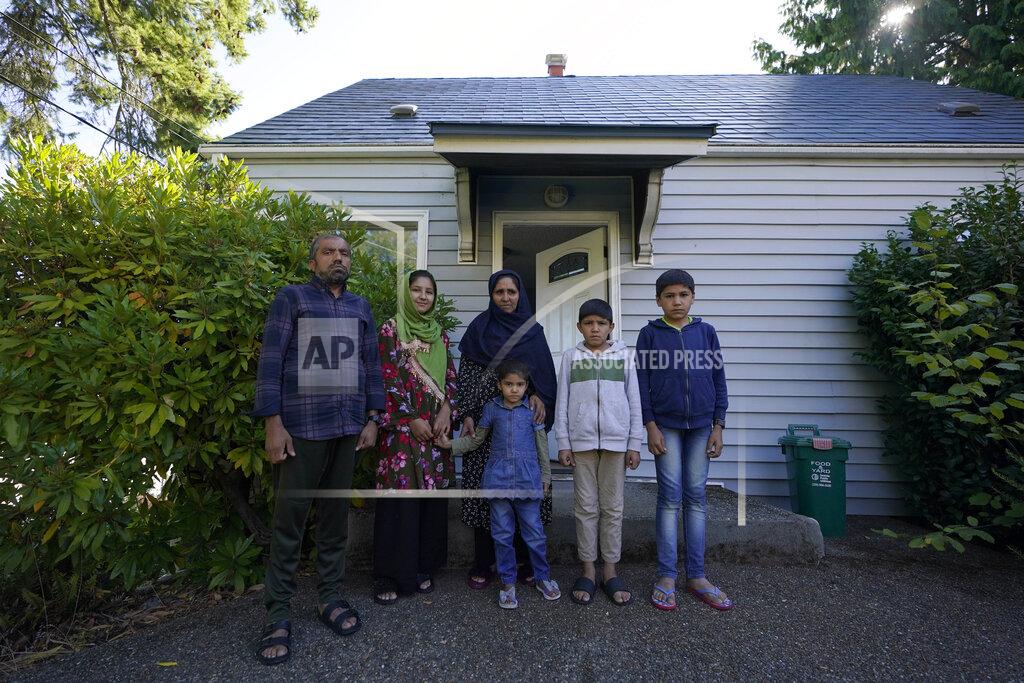 Ted S. Warren Abdul, left, who worked as a mechanic before he left Kabul, Afghanistan with his family about a month ago, poses for a photo, Thursday, Sept. 16, 2021, with his family in front of a rental house where they have been provided a place to stay in Seattle. The home is owned by Thuy Do, who was nine years old when her family arrived in the United States from Vietnam in the 1980s. Now Do and her husband have offered their vacant rental home to refugee resettlement groups to house newly arriving Afghans in need of a place to stay. (AP Photo/Ted S. Warren)