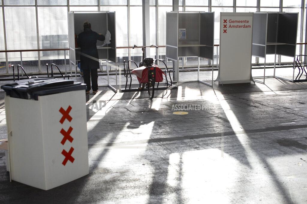 Peter Dejong A woman casts her ballot in ride through polling station for bicycles in Amsterdam, Netherlands, Monday, March 15, 2021. Polling stations opened across the Netherlands early Monday in a general election that has been spread over three days to allow people to vote safely during the coronavirus pandemic. (AP Photo/Peter Dejong)