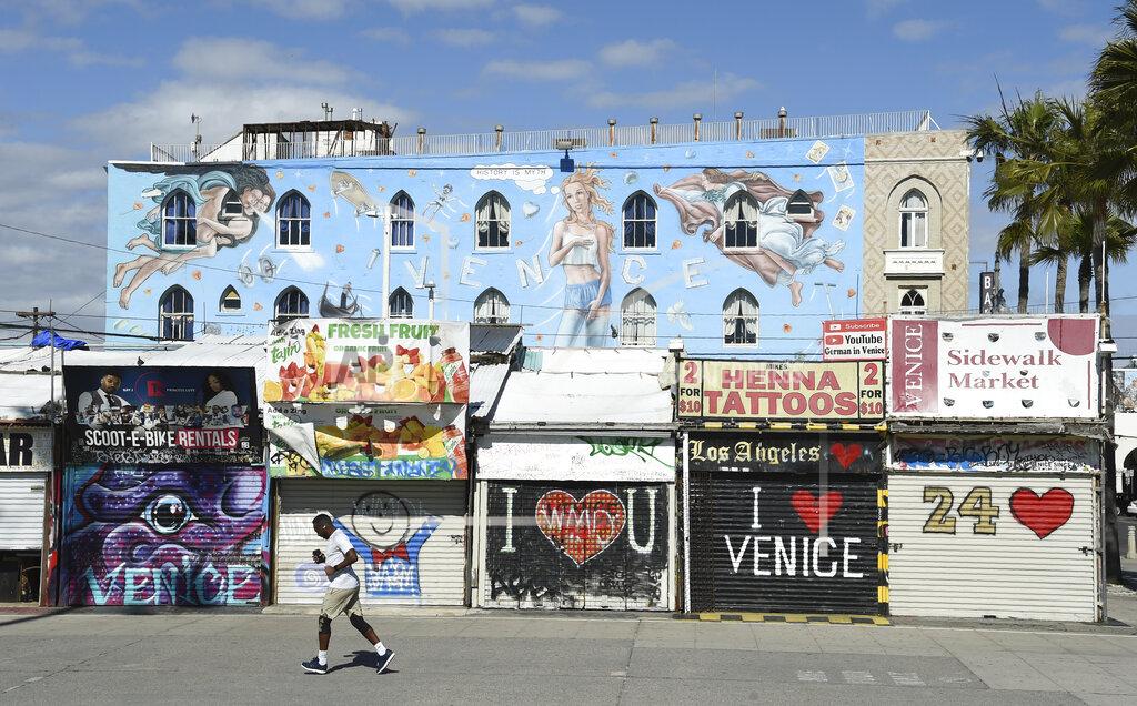 Chris Pizzello FILE - In this March 23, 2020, file photo, a jogger runs past shuttered shops along Venice Beach Boardwalk, in Los Angeles. The coronavirus crisis is upending service businesses, and the crisis may permanently change the way Americans work, shop and socialize, even after the disease fades away. (AP Photo/Chris Pizzello, File)
