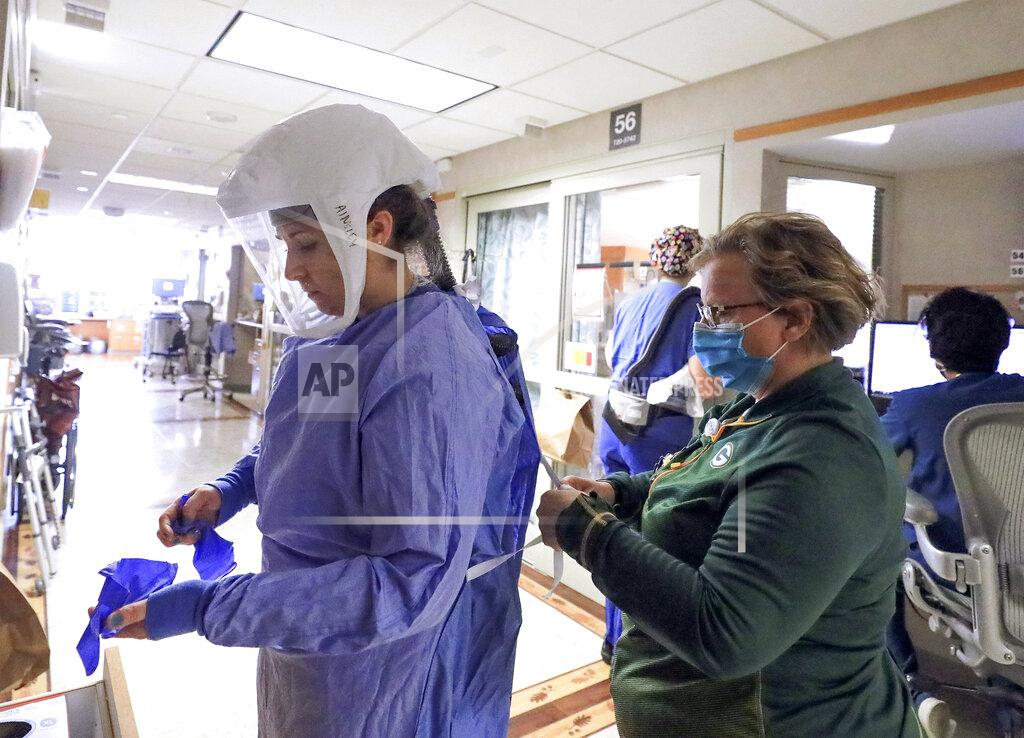 FILE - In this Nov. 5, 2020, file photo, Deb Dalsing, nurse manager of the COVID-19 treatment unit at UW Health assists nurse Ainsley Billesbach with her personal protective equipment at the hospital in Madison, Wis. Wisconsin spent at least $99 million on personal protective gear and medical equipment such as ventilators during the chaotic early months of the coronavirus pandemic, with almost all the money going to out-of-state suppliers, an Associated Press analysis shows. (John Hart/Wisconsin State Journal via AP, File)