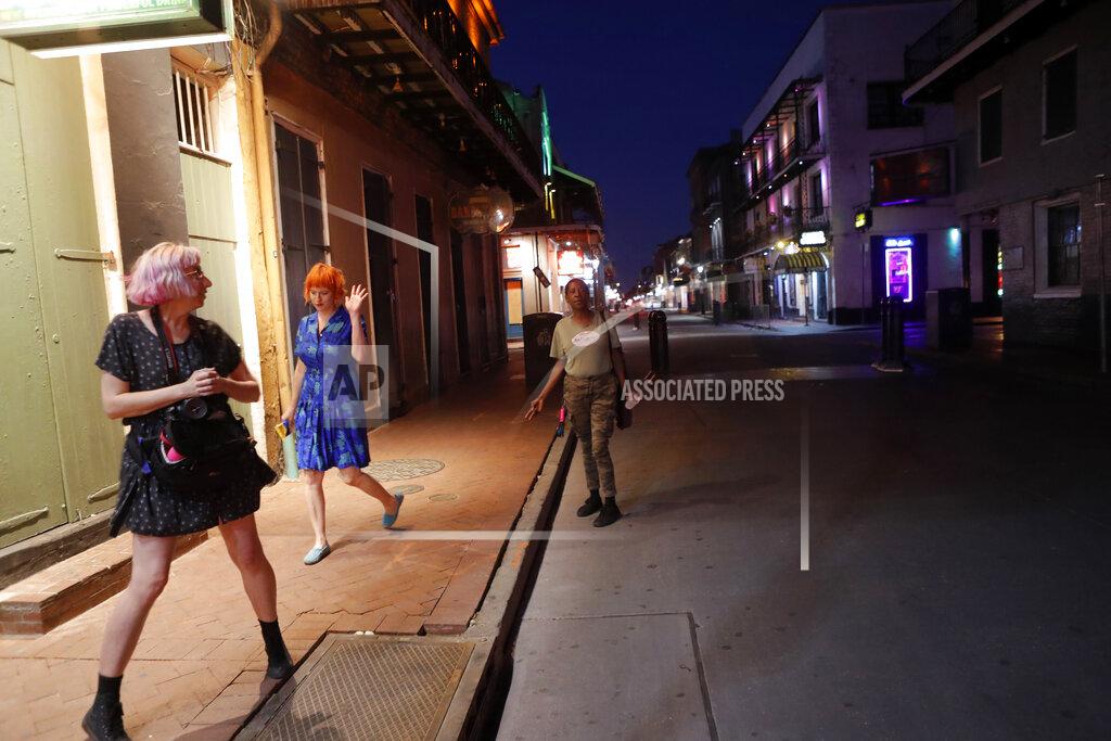 Gerald Herbert FILE - In this March 23, 2020 file photo, Jessica Fender, center, and Kerry Maloney, left, shy away from a woman asking for money after they felt she got too close, as the two exercise social distancing due to the new coronavirus outbreak, on a deserted Bourbon Street in New Orleans. Where political divides marred early recovery efforts after Hurricane Katrina in 2005, Louisiana is showing rare political unity in the fight against the new coronavirus. (AP Photo/Gerald Herbert, File)
