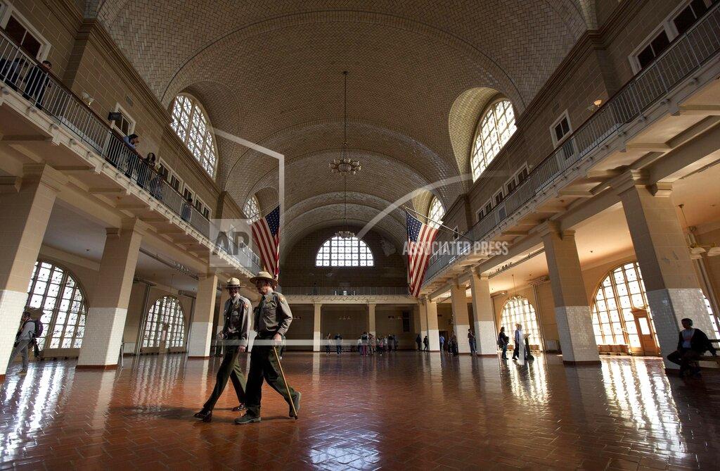 Julie Jacobson FILE - National Park Service rangers walk through the Great Hall at Ellis Island, on April 29, 2015, in New York. The location is featured in a collection of mini-essays by American writers published online by the Frommer's guidebook company about places they believe helped shape and define America. (AP Photo/Julie Jacobson, File)