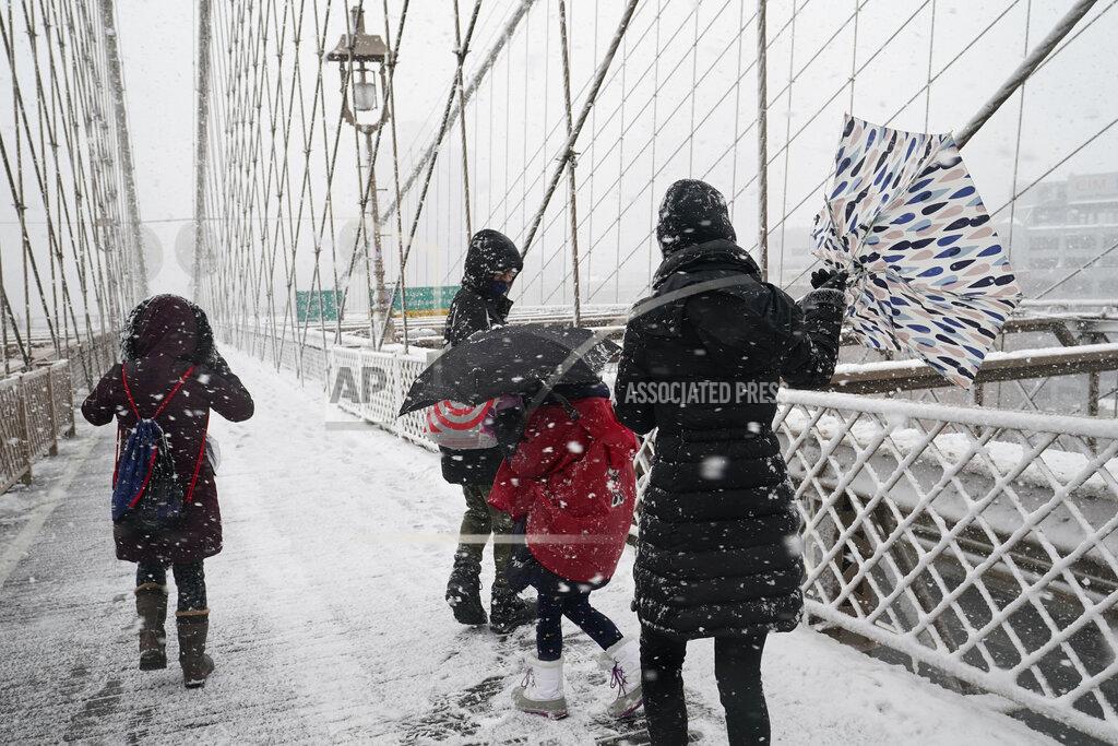 Kathy Willens A woman's umbrella turns inside out as she walks across the Brooklyn Bridge with family members during a snowstorm, Sunday, Feb. 7, 2021, in New York. (AP Photo/Kathy Willens)