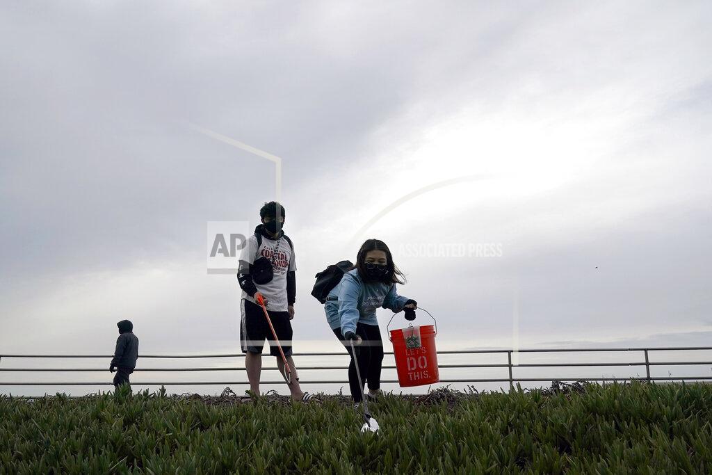 Jeff Chiu Pacifica Beach Coalition volunteers Alec Juntura, 21, foreground left, and Kimmy Tran, 20, pick up trash near Sharp Park Beach in Pacifica, Calif., Wednesday, March 17, 2021. Disposable masks, gloves and other personal protective equipment have safeguarded untold lives during the pandemic. They’re also creating a worldwide environmental problem, littering streets and sending an influx of harmful plastic into landfills and oceans. (AP Photo/Jeff Chiu)