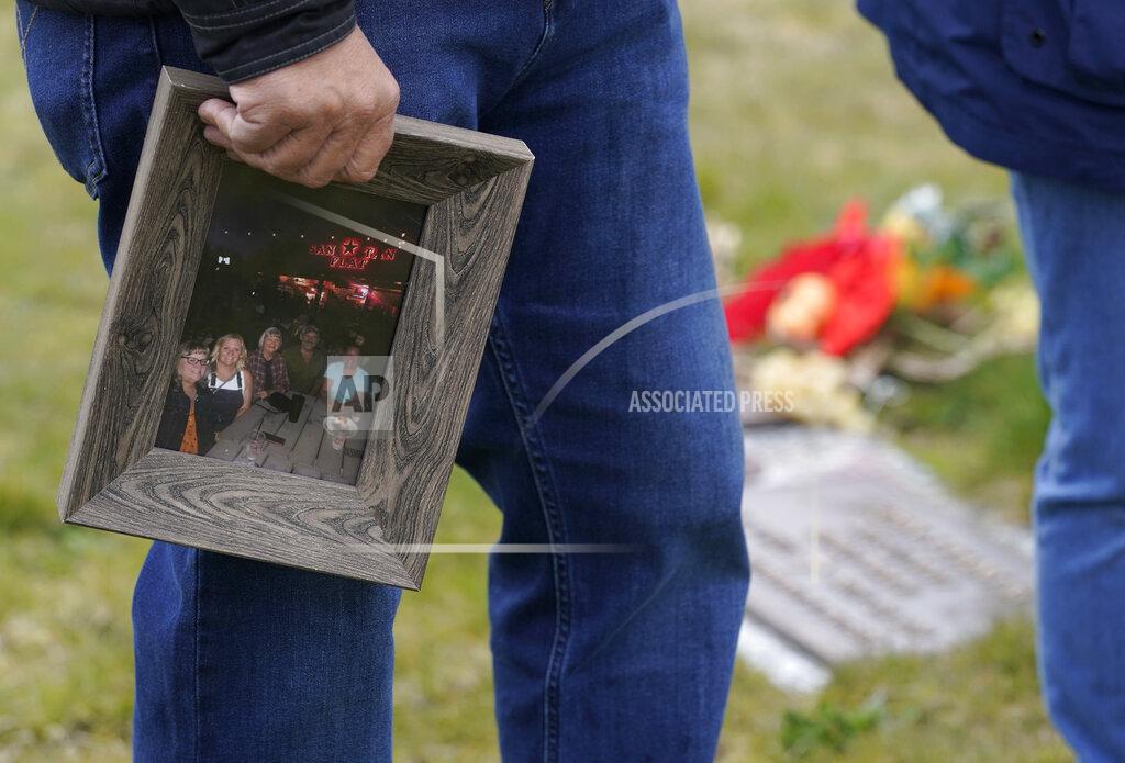 Joe Woodmansee holds a photo of the last time he and his three siblings were together with their mother, Carole Rae Woodmansee, as he visits Carole's grave, Saturday, March 27, 2021, at Union Cemetery in Sedro-Woolley, Wash., north of Seattle, prior to a memorial service. Carole died a year ago on the same date in 2020 — the day of her 81st birthday — from complications of COVID-19 after contracting it during a choir practice that sickened 53 people and killed two — a superspreader event that would become one of the most pivotal transmission episodes in understanding the virus. (AP Photo/Ted S. Warren)