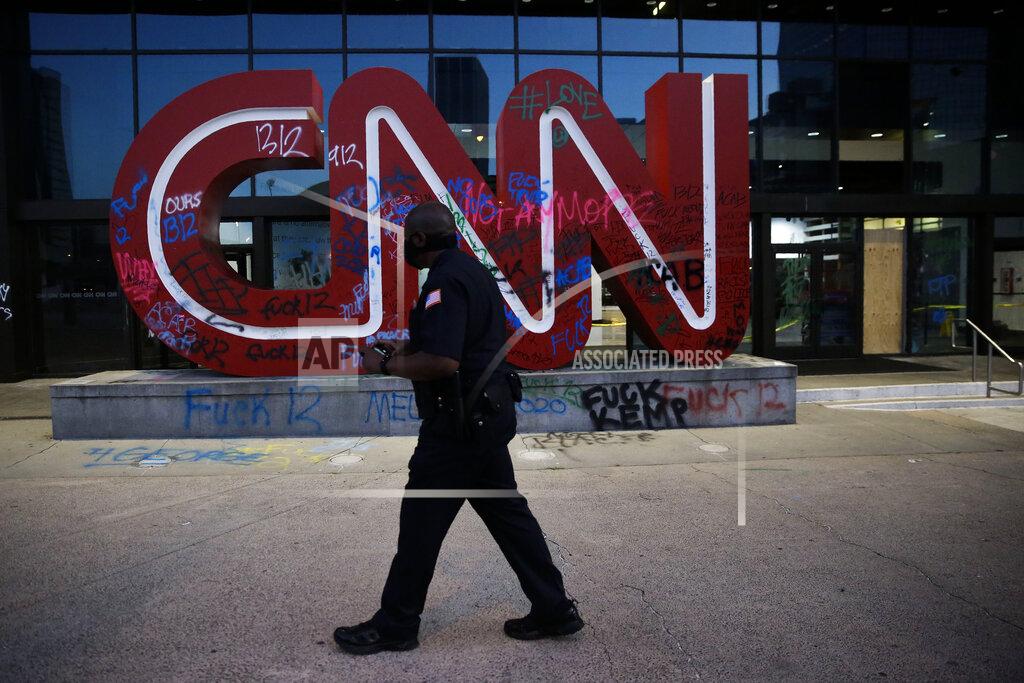 Brynn Anderson EDS NOTE: GRAPHIC CONTENT - A security guard walks in front of a damaged CNN sign at the CNN Center in the aftermath of a demonstration against police violence on Saturday, May 30, 2020, in Atlanta. (AP Photo/Brynn Anderson)