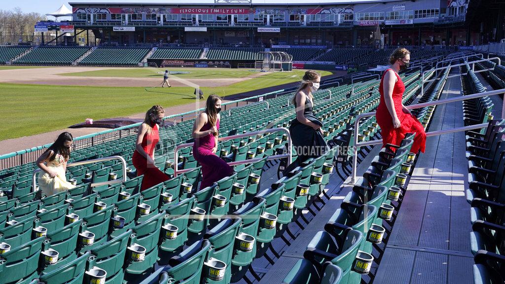 Charles Krupa While wearing their prom gowns, students walk through the stands along the third baseline at the New Hampshire Fisher Cats minor league baseball stadium in Manchester, N.H., on Monday, April 26, 2021. After a year without proms, school districts across the country are debating whether they can safely hold an event that many seniors consider a capstone to their high school experience. The nearly 300 student senior class of Manchester's Central High School are waiting to get approval from the city's board of health so they can have their prom at the outdoor venue, due to COVID-19 concerns. (AP Photo/Charles Krupa)