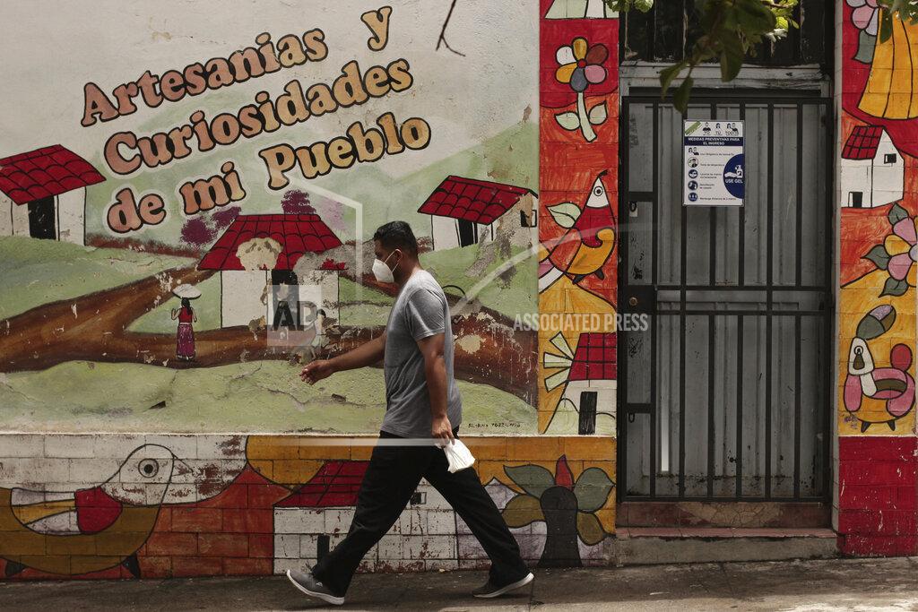 Salvador Melendez A pedestrian walks past a sign offering tips on safe social distancing and preventive measure to help curb the spread of the new coronavirus, in Santa Ana, El Salvador, Saturday, Aug. 22, 2020. After navigating legal snags and rigorous checks requiring they show they're in danger in Central America, refugees who were approved to come to the U.S. have faced more delays as the pandemic grounded flights, canceled final interviews and closed clinics that conduct needed medical exams. (AP Photo/Salvador Melendez)