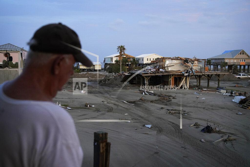 John Locher Kelty Readenour stands on his porch overlooking a sand and debris-covered roadway and homes destroyed by Hurricane Ida, Monday, Sept. 6, 2021, in Grand Isle, La. (AP Photo/John Locher)