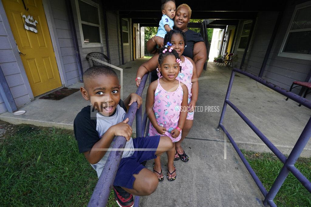 Rogelio V. Solis Brianne Epps of Jackson, Miss., 28, background, is a single mother with sons Micah Epps, 4, in front, and Nolan Epps, 11 months in her arms and daughters Laila Barnes, 6, second from left, and Kaylee Barnes, 8, center, outside her apartment complex in Jackson, Miss., Wednesday, July 21, 2021. Epps earns $9 an hour working with infants and toddlers in a childcare center, but she has a bigger dream of operating a soul food catering business. (AP Photo/Rogelio V. Solis)