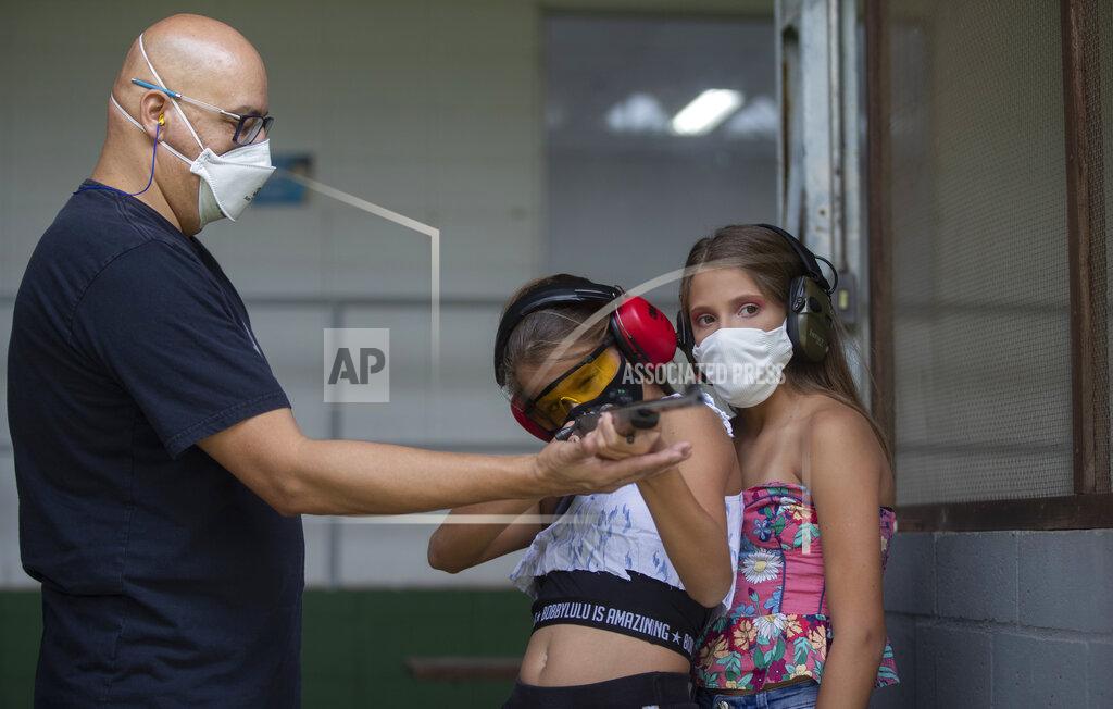 Andre Penner Instructor Robson de Oliveira trains his 10-year-old twin daughters Lorena, center, and Lara, how to properly shoot a firearm at a shooting range in Americana, in the Sao Paulo state of Brazil, Saturday, March 6, 2021. As authorized by two of the most divisive presidential decrees, average Brazilians will be able to own six guns, up from four currently, and carry two simultaneously. (AP Photo/Andre Penner)