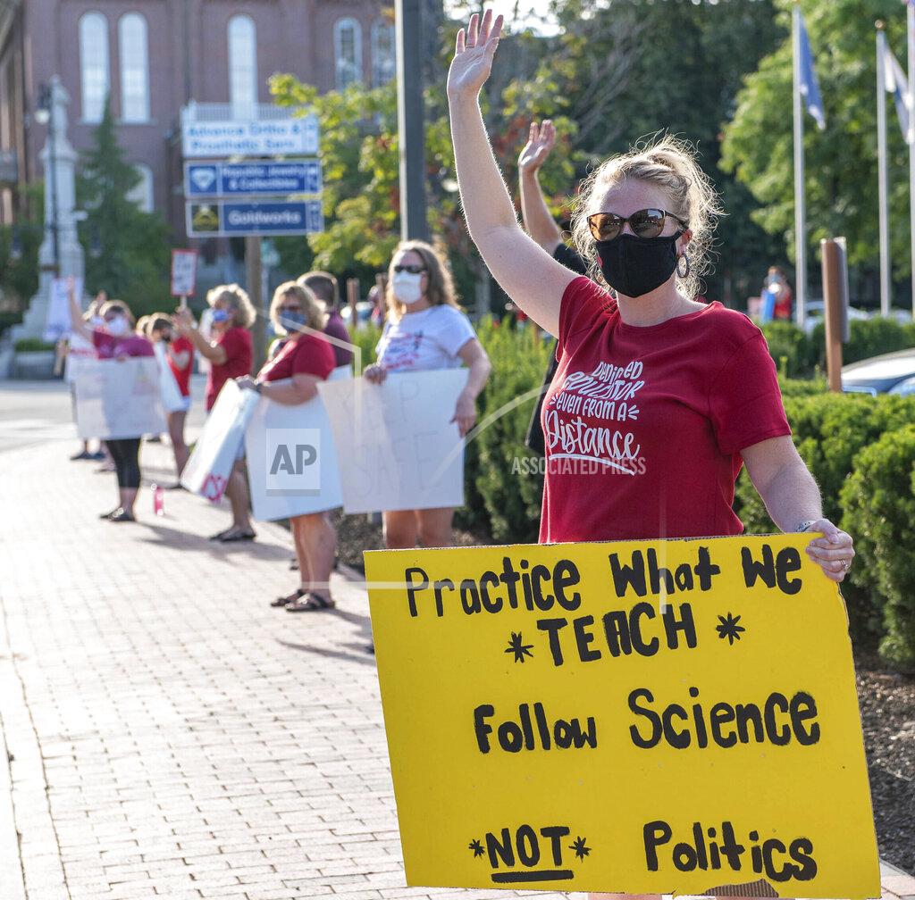 Andree Kehn Kristi McCarthy, a teacher at the Walton School waves to traffic on Court Street in Auburn, Maine on Wednesday, Aug. 12, 2020 evening while she participates in a stand-in to advocate for a return to school plan that takes a more cautious approach to COVID-19 prevention. (Andree Kehn/Sun Journal via AP)