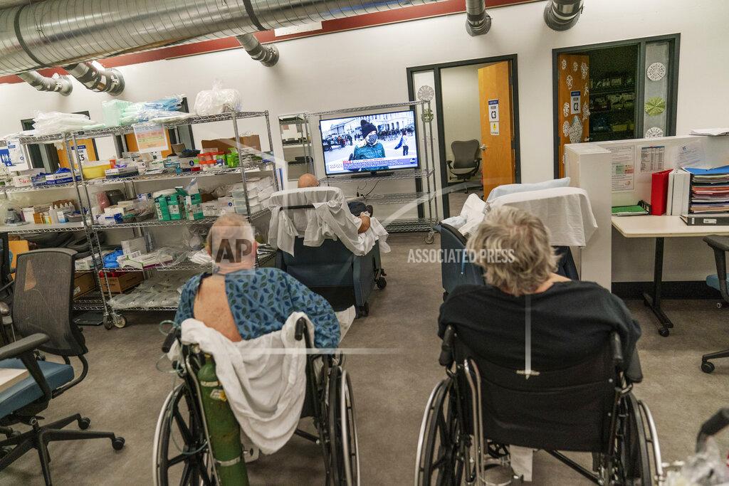David Goldman COVID-19 patients watch television in a common area of a field hospital set up to handle a surge of COVID-19 patients Wednesday, Jan. 6, 2021, in Cranston, R.I. Unlike in a regular hospital ward, where COVID patients can't leave their rooms, patients here are free to roam. (AP Photo/David Goldman)