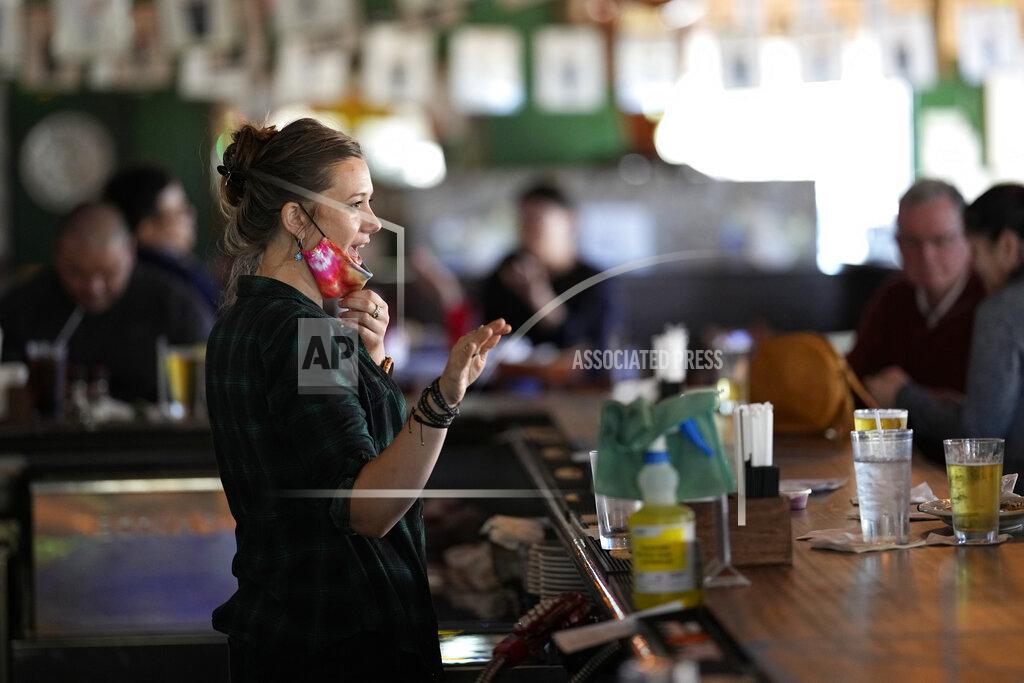 David J. Phillip Bartender Alyssa Dooley talks with customers at Mo's Irish Pub, Tuesday, March 2, 2021, in Houston. Texas Gov. Greg Abbott announced that he is lifting business capacity limits and the state's mask mandate starting next week. (AP Photo/David J. Phillip)