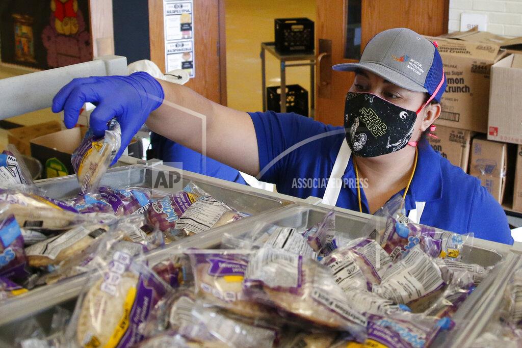 Brenda Linares reaches for sandwiches to pack into lunches at Prairie Queen elementary school as lunches and instructional packets are distributed Monday, April 20, 2020, in Oklahoma City. Oklahoma City Schools are operating remotely through the end of the school year due to COVID-19 concerns. (AP Photo/Sue Ogrocki)