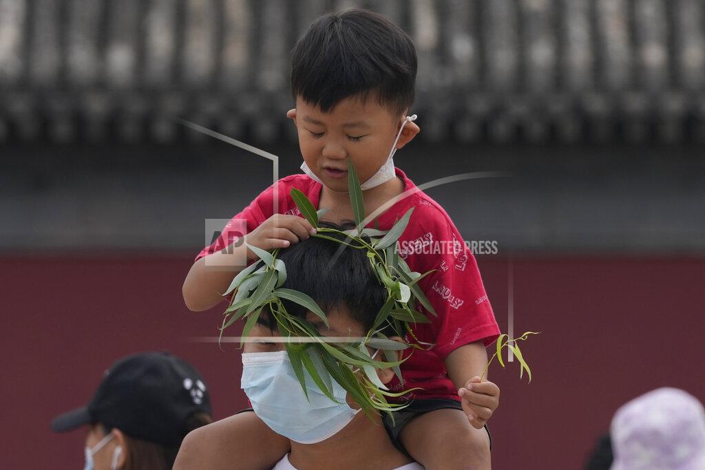 Ng Han Guan A child puts a wreath over the head of a man wearing a mask in Beijing Tuesday, Aug. 3, 2021. The coronavirus’s delta variant is challenging China’s costly strategy of isolating cities, prompting warnings that Chinese leaders who were confident they could keep the virus out of the country need a less disruptive approach. (AP Photo/Ng Han Guan)