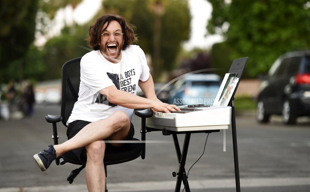 Chris Pizzello In this May 9, 2020 photo, musician Adam Chester mugs for a portrait on his street after performing his weekly neighborhood concert in the Sherman Oaks section of Los Angeles. Normally, Chester is a surrogate Elton John, who sings and plays the rock superstar's parts at rehearsals. With that work on hold, Chester has been giving concerts to his neighbors from a safe social distance in front of his house. (AP Photo/Chris Pizzello)