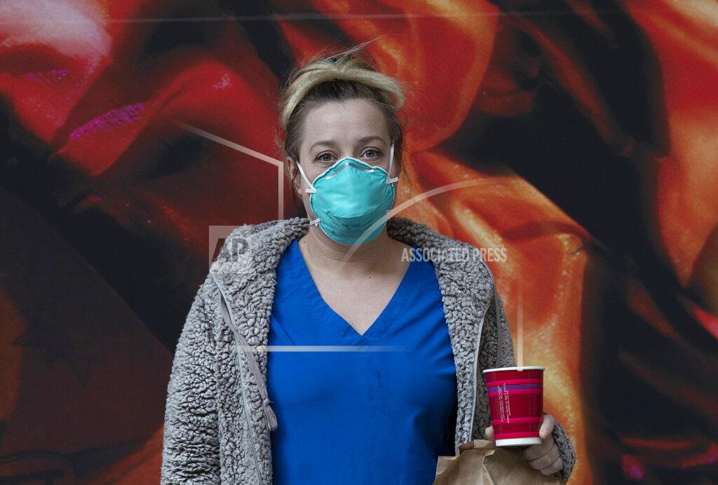 \Nurse Jessica Upton, of Huntsville, Ala. poses in front of a display for the Broadway show "Moulin Rouge" before taking a bus from a Times Square hotel to Harlem Hospital, Wednesday, April 15, 2020, in New York. A collapsing hotel industry that long feasted on large gatherings like conventions and weddings has reinvented itself in the nation's pandemic hotspots, providing homes away from home for America's newest heroes. (AP Photo/Mark Lennihan)