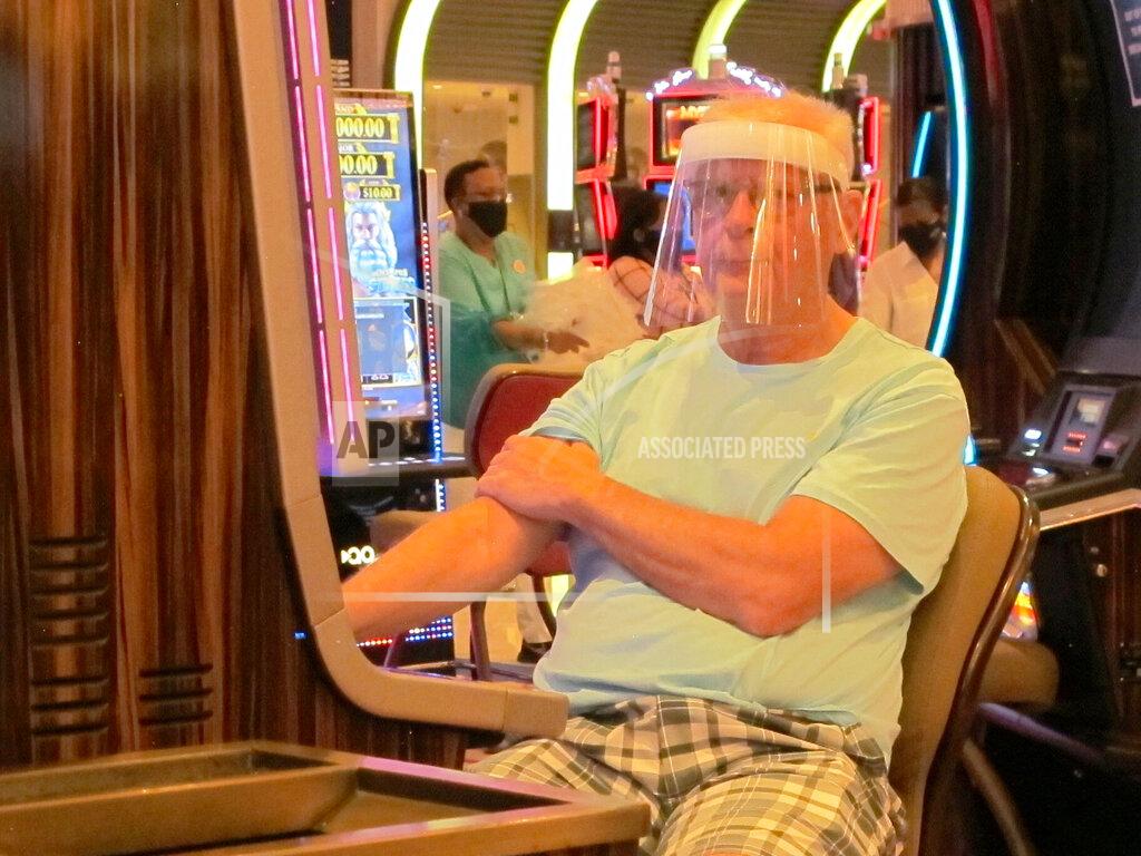 Wayne Parry A gambler wears a face shield while playing a slot machine at the Hard Rock casino in Atlantic City N.J. on July 2, 2020, the first day it was allowed to reopen during the coronavirus pandemic. Figures released on April 9, 2021 show Atlantic City's nine casinos collectively saw their gross operating profits decline by more than 80% in 2020.(AP Photo/Wayne Parry)