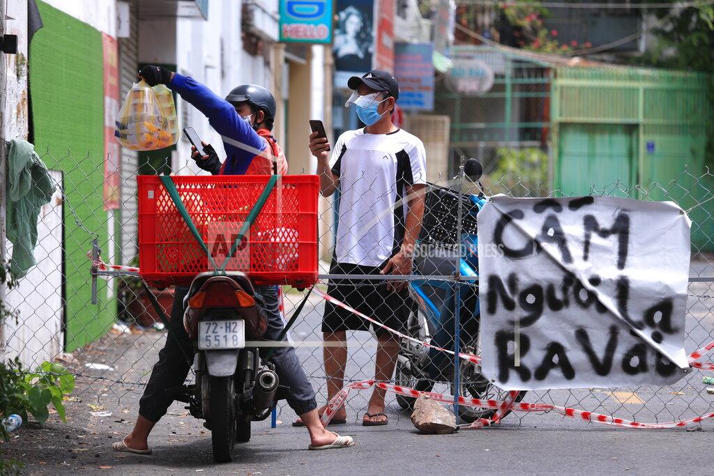 Hau Dinh A delivery man hands over food order to another at a fence set up block traffic in Vung Tau, Vietnam, Monday, Sept. 13, 2021. The sign at right reads "No non-resident". The roadblocks and barricades make the streets of this southern Vietnamese city look like they did during the war that ended almost 50 years ago. But this time, the battle is being fought against the rampaging coronavirus.(AP Photo/Hau Dinh)