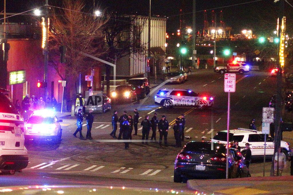 Ted S. Warren Tacoma Police and other law enforcement officers stand in an intersection near the site of a car crash Saturday, Jan. 23, 2021, in downtown Tacoma, Wash. At least one person was injured when a police car plowed through a crowd of people Saturday night who were watching a downtown street race, the Tacoma News-Tribune reported. (AP Photo/Ted S. Warren)