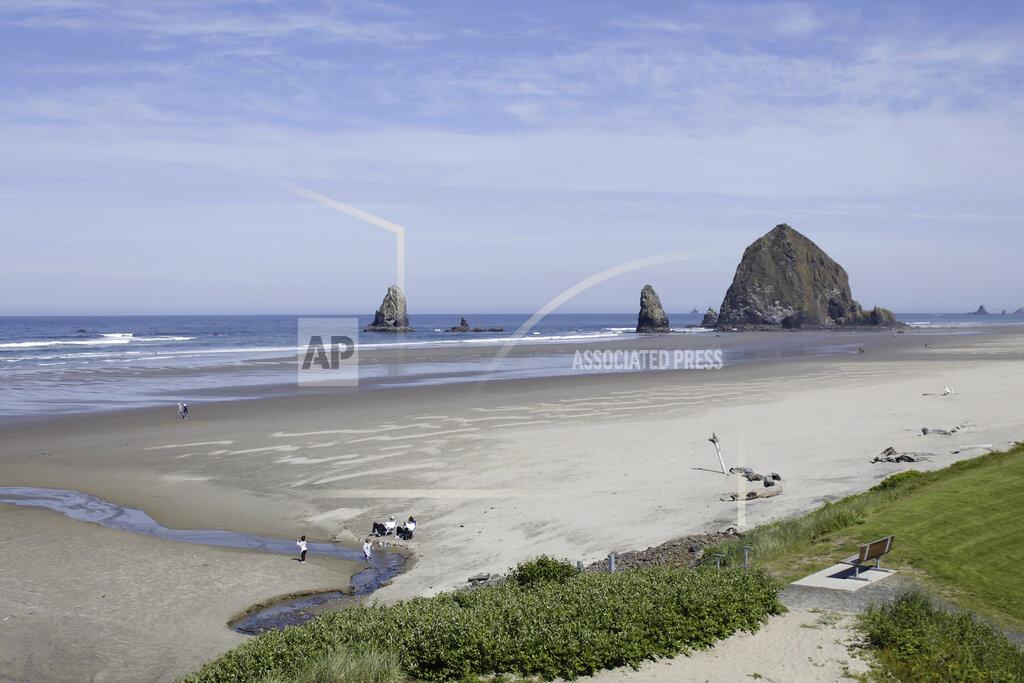 Gillian Flaccus FILE - This Thursday, May 28, 2020, file photo shows Haystack Rock is seen in the distance from a balcony of The Ocean Lodge, in Cannon Beach, Ore., during the coronavirus outbreak. The sand was packed on a recent sunny day at this upscale beach town on Oregon's coast, but signs of the state's cautious approach to the pandemic were still everywhere. It was a sharp contrast to places such as Florida or Texas, where many COVID-19 restrictions have been lifted for weeks. (AP Photo/Gillian Flaccus, File)