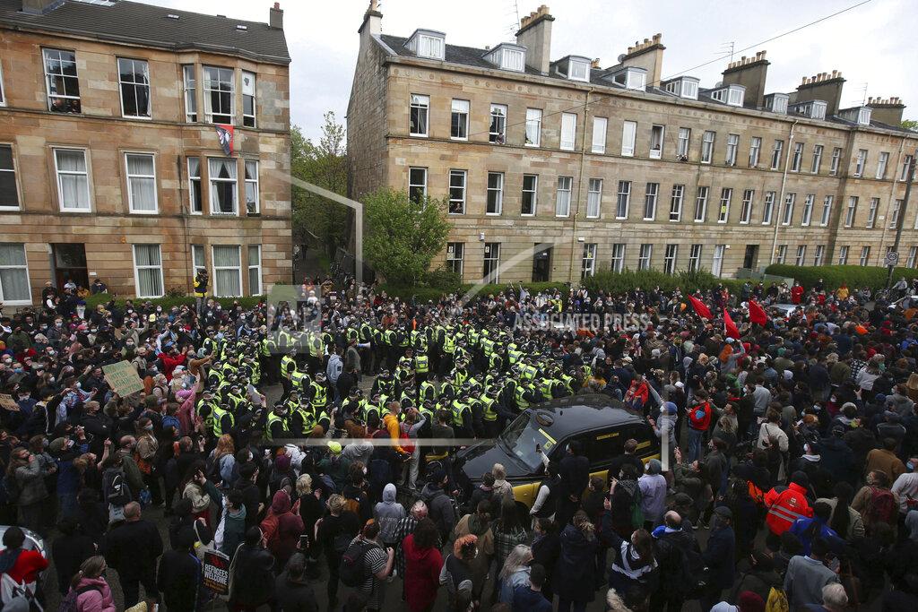 Andrew Milligan Two men stand surrounded by police and protesters, after being released from an Immigration Enforcement police van accompanied by lawyer Aamer Anwar and Mohammad Asif, director of the Afghan Human Rights Foundation, in Glasgow, Scotland, Thursday May 13, 2021. Some hundreds of protesters blockaded the street in Glasgow on Thursday in a seven-hour standoff which successfully forced the release of two men detained by U.K. immigration authorities. (Andrew Milligan/PA via AP)