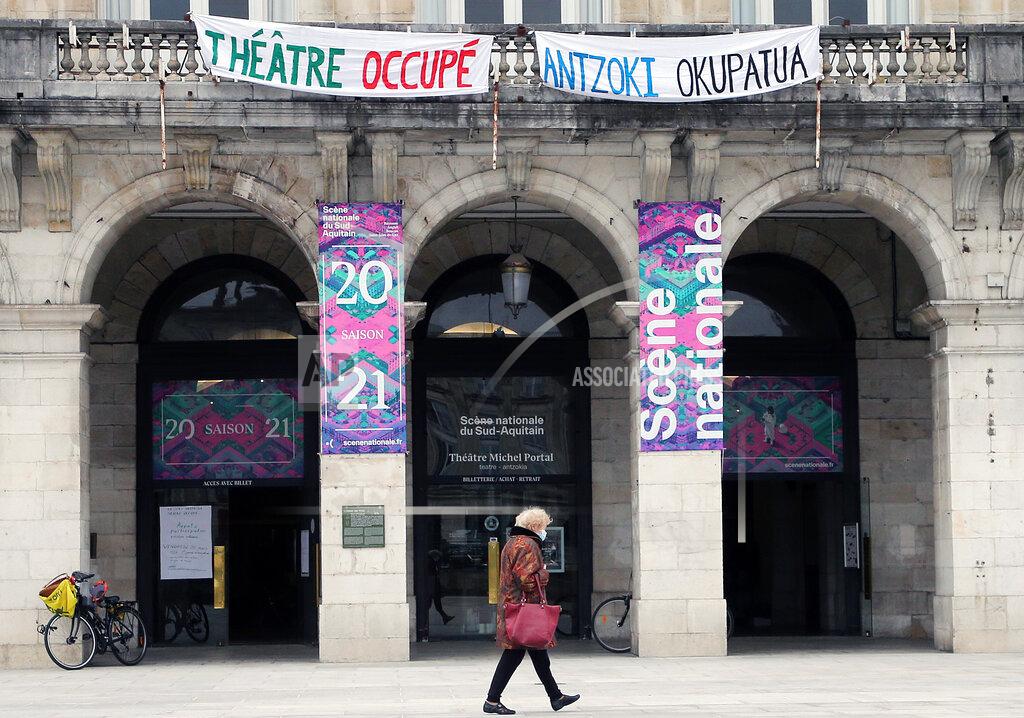 Bob Edme A woman walks past a theater with signs showing it occupied by culture workers, actors students and theater employees in Bayonne, southwestern France, Friday, March 26, 2021. French theaters, cinemas, museums and tourist sites have been closed for much of the past year as part of government virus protection measures, and no reopening plans have been announced. (AP Photo/Bob Edme)