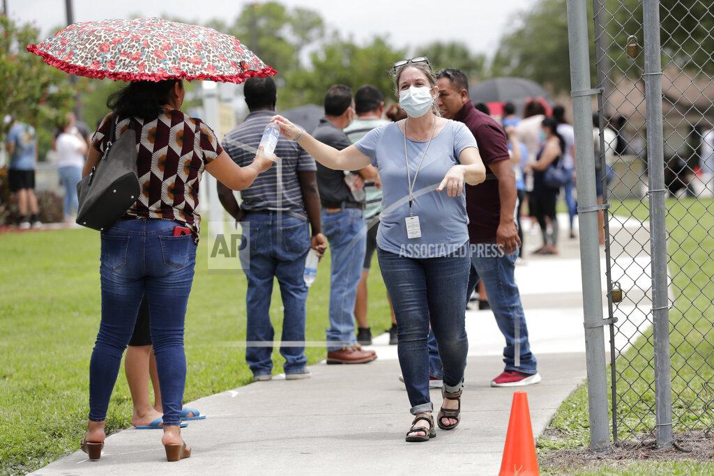 Lynne Sladky In this Sunday, June 7, 2020, photo, Gretel Cacerces, right, passes out bottled water to those standing in line for COVID-19 testing at the Florida Department of Health in Collier County amid the new coronavirus pandemic in Immokalee, Fla. Even as the pace of new cases has moderated in the state of Florida, this poor farmworking town in rural Florida is in the throes of an outbreak. (AP Photo/Lynne Sladky)