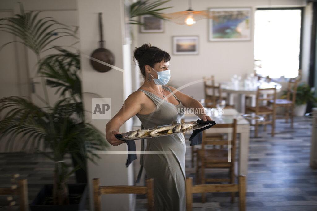 Daniel Cole A waitress wearing a face mask to protect against coronavirus carries out a plate of fish to serve at a seafood restaurant in Marseille, southern France, Tuesday, June 2, 2020. The French way of life resumes Tuesday with most virus-related restrictions easing as the country prepares for the summer holiday season amid the pandemic. (AP Photo/Daniel Cole)