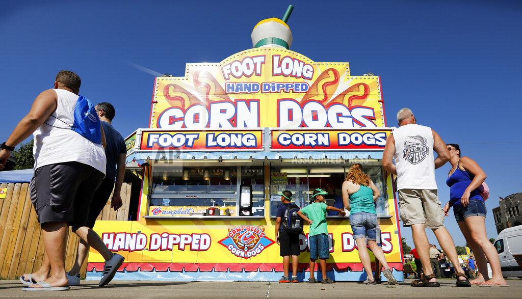 Charlie Neibergall FILE - In this Aug. 9, 2018 file photo, Iowa State fairgoers line up to get a corn dog at a concession stand during the opening day of the Iowa State Fair in Des Moines, Iowa. With coronavirus cases rising throughout Iowa and around the nation, health experts are becoming increasingly worried about next month's Iowa State Fair, which will bring more than 1 million people to Des Moines. (AP Photo/Charlie Neibergall, File)