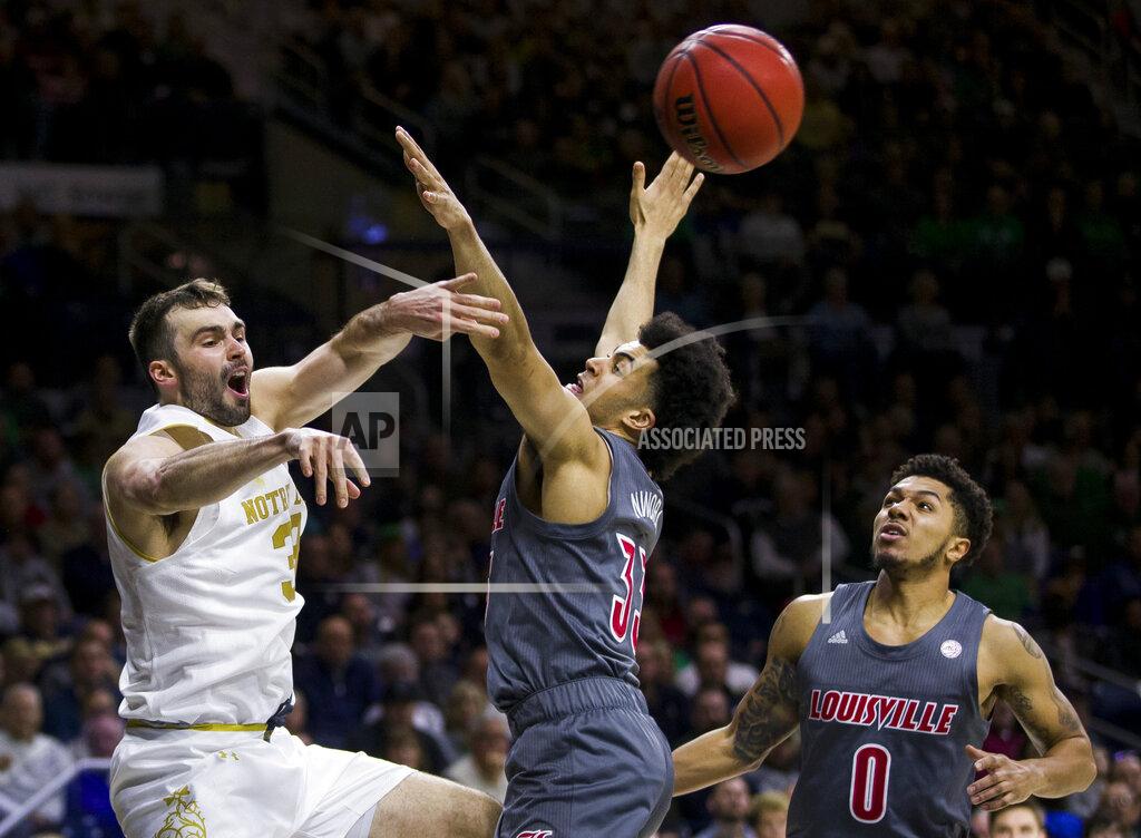 Robert Franklin Notre Dame's John Mooney, left, passes around Louisville's Jordan Nwora (33) and Lamarr Kimble (0) during the second half of an NCAA college basketball game Saturday, Jan. 11, 2020, in South Bend, Ind. Louisville won 67-64. (AP Photo/Robert Franklin)