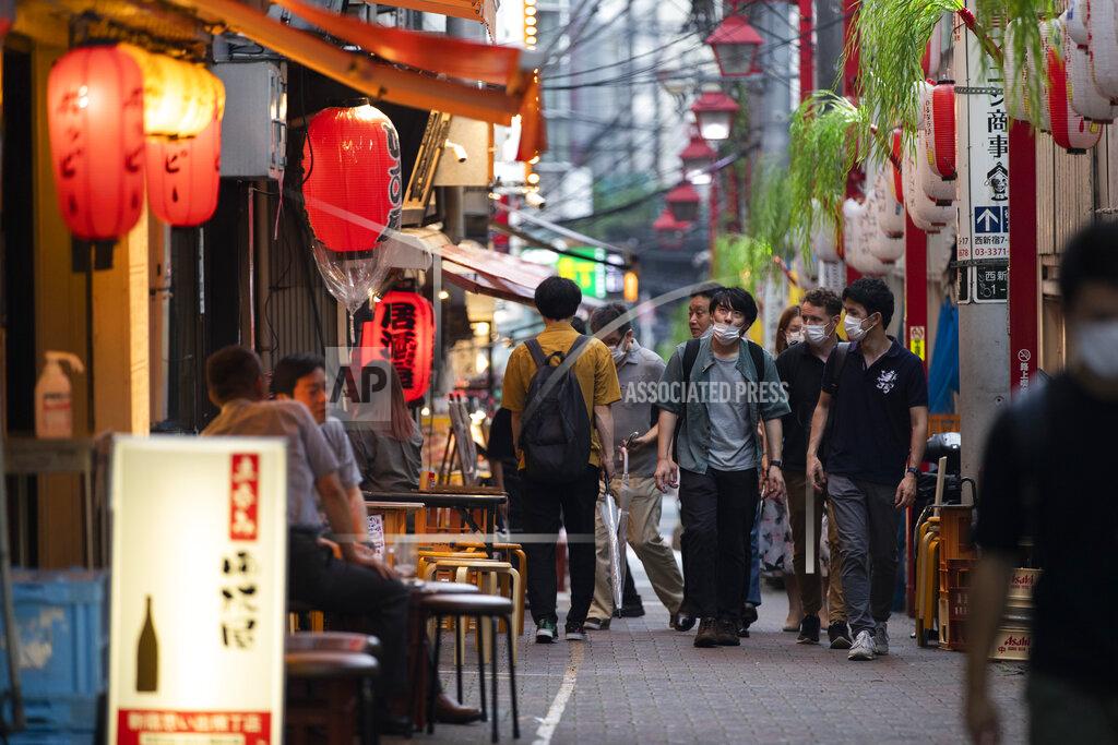 People walk around before getting into a restaurant/bar in Tokyo on Friday, July 9, 2021. Tens of thousands of visiting athletes, officials and media are descending on Japan for a Summer Olympics unlike any other. There will be no foreign fans, no local fans in Tokyo-area venues. A surge of virus cases has led to yet another state of emergency. And a local vaccination campaign is struggling to keep up.(AP Photo/Hiro Komae)