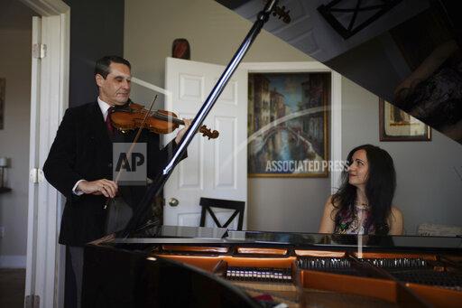 Musicians David Shenton and Erin Shields perform inside their home in the Queens borough of New York on March 30, 2021. The married couple have led virtual concerts from their living room to raise thousands of dollars for the Mosaic West Queens Church food pantry, where they volunteer every weekend. (AP Photo/Emily Leshner)