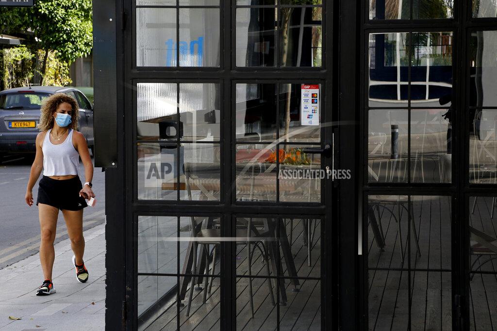 Petros Karadjias A woman wearing protective face mask walks outside of a closed cafe amid COVID-19 pandemic restrictions government in central capital Nicosia, Cyprus, Thursday, May 6, 2021. Cyprus has unveiled a phased rollback of COVID-19 lockdown restrictions over the next month including a shortened curfew and a reopening of all schools next week, but will enforce the compulsory display of proof of vaccination, virus testing or convalescence from the disease in areas were people gather in numbers, including restaurants and churches. (AP Photo/Petros Karadjias)