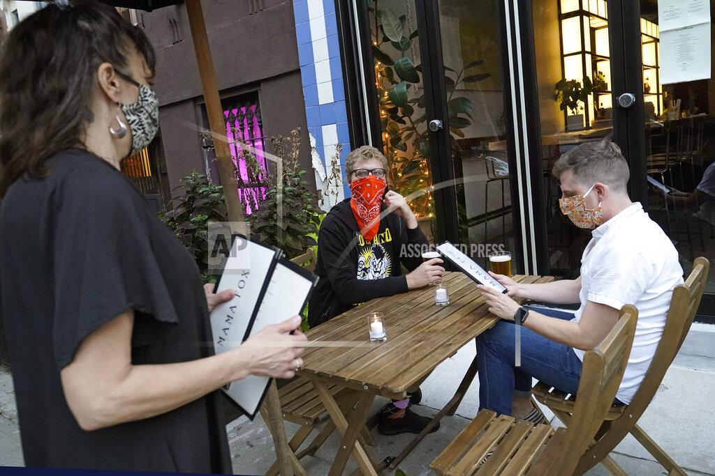 Kathy Willens FILE — In this Sept. 29, 2020 file photo, restaurant owner Samantha DiStefano, left, of Mama Fox, prepares to hand menus to patrons dining outside at her Brooklyn establishment, in New York. The coronavirus and the drastic measures put in place by government officials to try to control its spread had a severe toll on many small businesses in the U.S. Restaurants, hair salons, event planners and other businesses that rely on people being in close proximity were particularly hard-hit, as were those tied to tourism. (AP Photo/Kathy Willens, File)