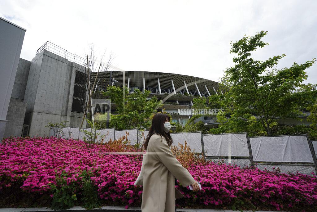 Eugene Hoshiko A woman wearing a protective mask to help curb the spread of the coronavirus walks near the Japan National Stadium, where opening ceremony and many other events are planned for postponed Tokyo 2020 Olympics Tuesday, April 6, 2021, in Tokyo. Many preparations are still up in the air as organizers try to figure out how to hold the postponed games in the middle of a pandemic. (AP Photo/Eugene Hoshiko)