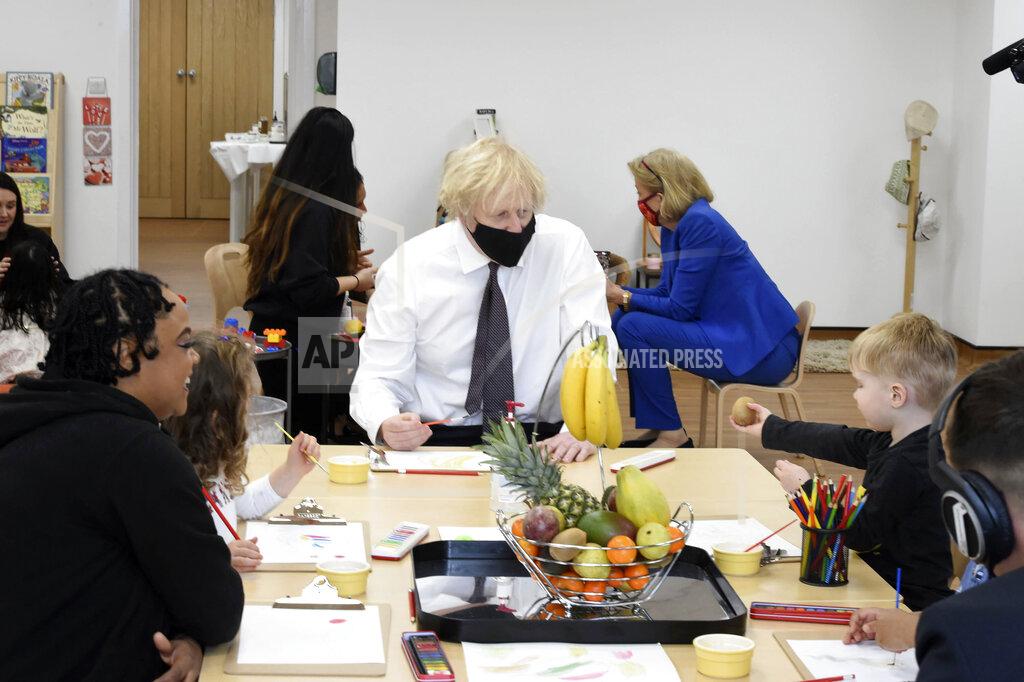 Jeremy Selwyn British Prime Minister Boris Johnson, center, sits with children drawing of a bunch of bananas during a visit to the Monkey Puzzle Nursery in Greenford, west London, Thursday, March 25, 2021. (Jeremy Selwyn/Pool Photo via AP)